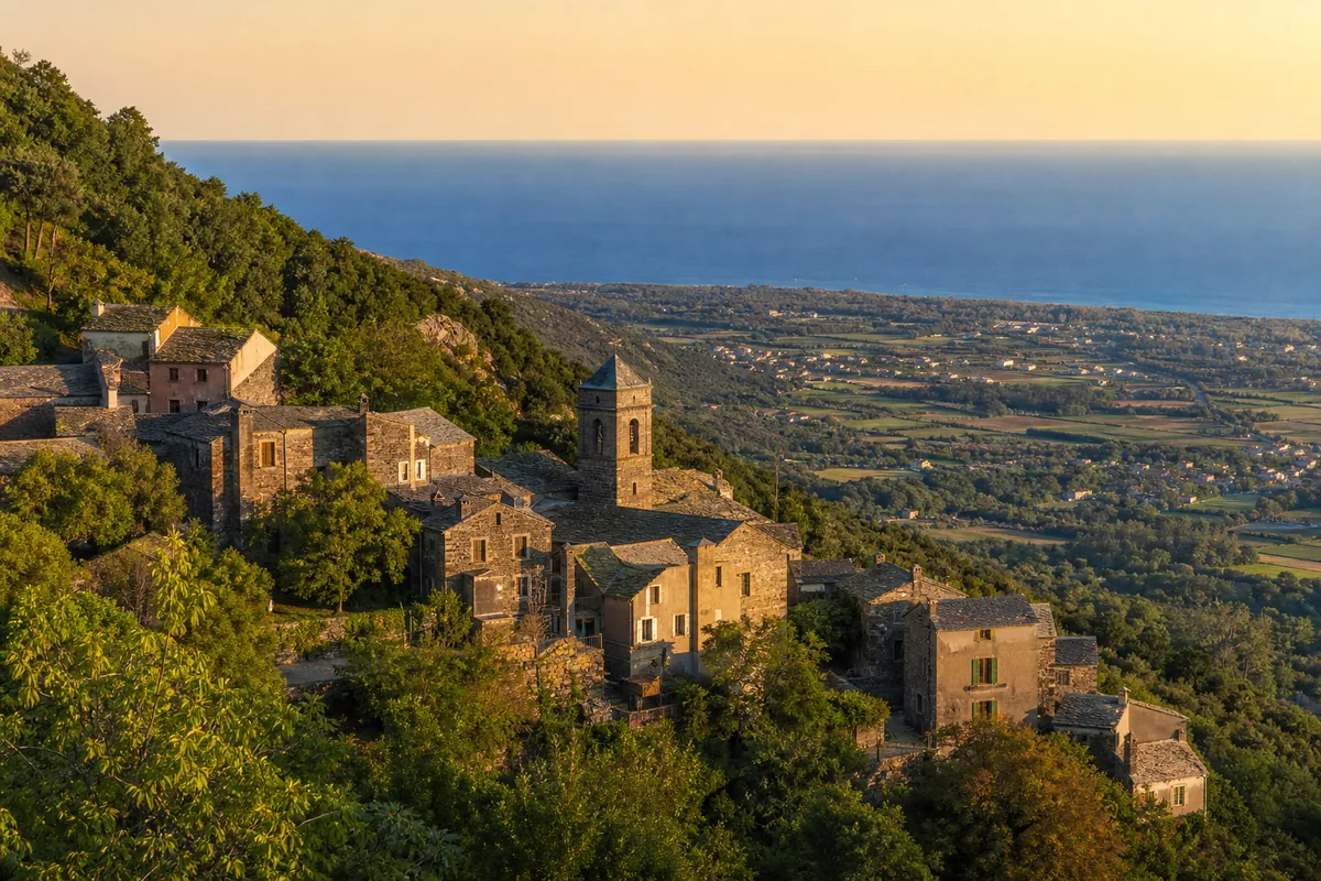 Village corse en pierre perché sur une colline boisée avec vue sur la plaine et la mer en arrière-plan